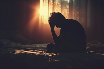 Silhouette of a young person sitting on the edge of a bed with head bowed, portraying the internal struggle with depression and stigma associated with seeking mental health help