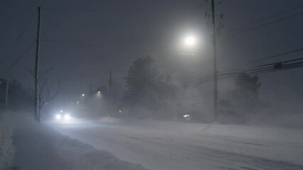 Car traffic on a winter road during a heavy snow storm with gusty winds at night in Dartmouth, Canada , 2023. Ice on the road and poor visibility during snowfall on the road with cars.