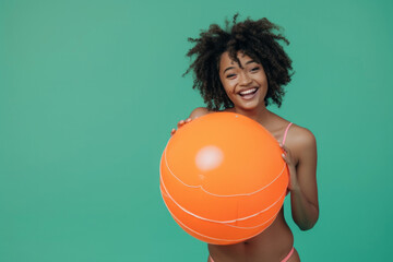 Funny young happy African American woman in swimsuit having fun holding inflatable ball and going...