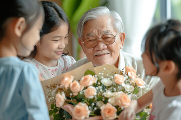 Happy Asian grandfather receives birthday presents from his loving family. Children together with grandmother give grandpa a card and a bouquet of beautiful flowers