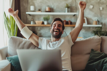 Man with an arm injury relaxing at home. Happy man with a sling on his broken arm sitting on the sofa, watching a funny movie on a laptop computer and laughing.