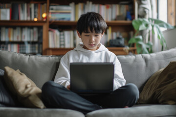Young ethnic Japanese Boy teenager uses laptop to chat with friends and use social networks on Internet sits on sofa with portable computer on lap. Digital addiction