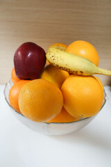 close up of a rotten banana, six oranges and an apple in a glass bowl