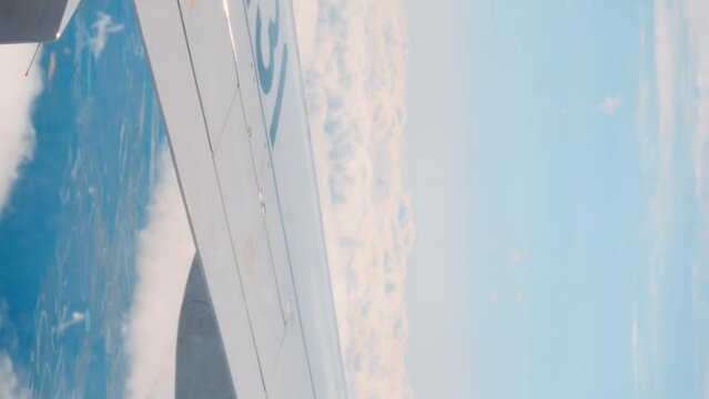View from airplane window captures plane wing blue sky vertical video View from airplane window looking into air travel's beauty. View from airplane window reveals majestic clouds vast skies.