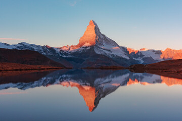 Colorful sunrise on Stellisee lake. Snowy Matterhorn peak with red light in clear water reflection....