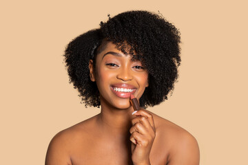 Young black woman applying lipstick with cheerful smile