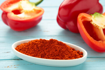 Paprika powder in plate with fresh red pepper on blue background.