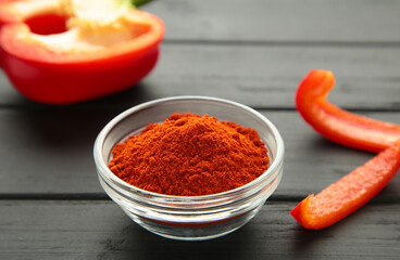 Paprika powder in plate with fresh red pepper on black background.