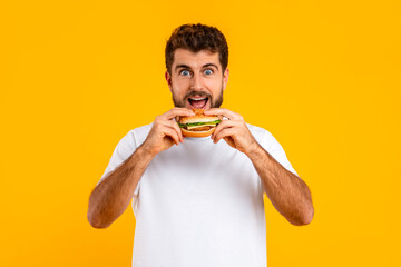 Portrait of joyful bearded man taking big bite of cheeseburger