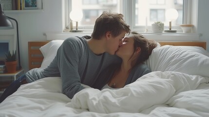 Obraz premium Romantic young couple kissing on soft white pillows under bright covers in a cozy morning bedroom