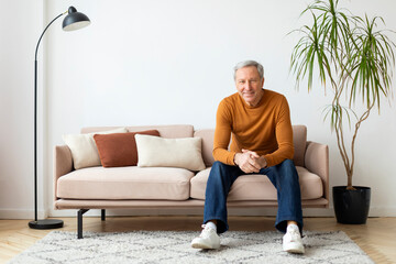 Positive retired european man sitting on couch in living room