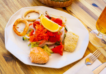 Appetizing seafood dish of grilled fish steaks and squid rings with fresh vegetable salad and lemon