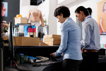 Diverse employees working with cardboard boxes, preparing customers orders for delivery in modern boutique. Store workers checking shippign detalis on computer, working with stylish clothes
