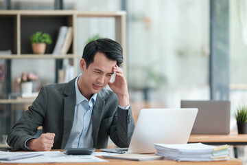 Fototapeta premium Young Stressed Out Businessman Using Laptop Computer in Modern Office. Manager Thinks About Successful Financial Ideas. Happy Man Smiling About Finding Problem Solving Solutions for Company.