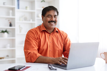 Cheerful mature indian businessman working on laptop at office