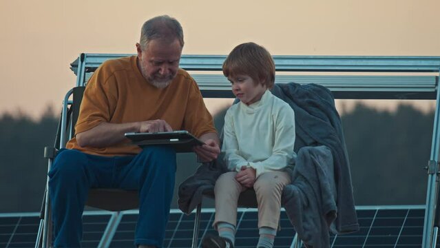 Evening twilight envelops the solar plant as a boy and his grandpa engage with a tablet atop their camper