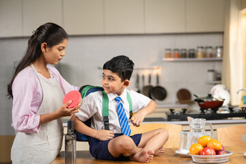 Caring Indian mother preparing kid for school by placing lunch box and water in bad - concept of responsibility, parental caring and back to school