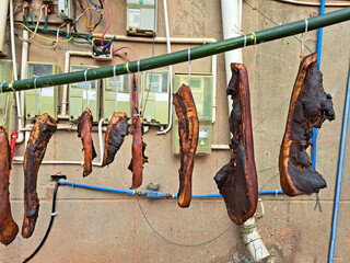 Close-up of large pieces of pork or beef meat hanging on a bamboo pole for curing process on city street at Chengdu, China. Sichuan smoked cured meat from traditional chinese cuisine