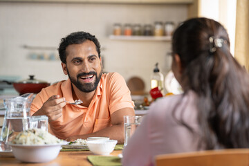 Shoulder shot of Married Indian couples talking together while eating lunch at home - concept of family bonding, relationship conversation and spending time