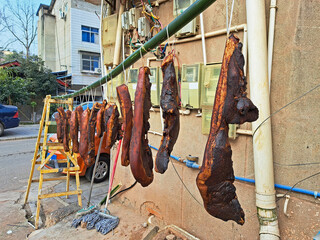 Many large pieces of smoked pork meat hanging on a bamboo pole of wooden rack for curing process in...