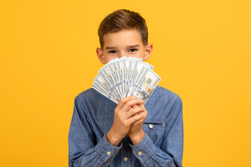 Smirking teenage boy hiding behind fan of dollar bills cash