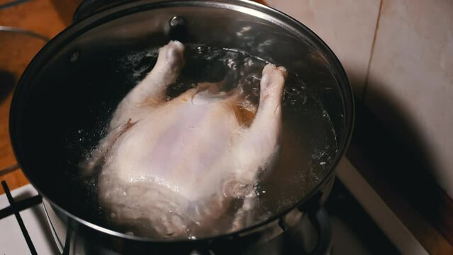 Cooking a Whole Chicken Carcass in a Pot of Boiling Water in a Home Kitchen. Close up. Rich chicken broth, broiler chicken leg soup. Smoke, steam. Homemade lunch or dinner. Poultry meat dishes. Food.