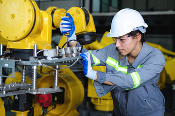 Caucasian female robot engineer wearing helmet and safety glasses using screwdriver to tighten...