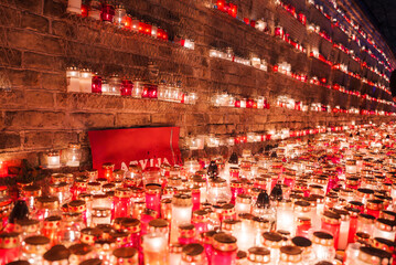 Rows of red and white candles, Latvia's colors, light a solemn scene with a central red flag marked LATVIJA. Their warm glow on bricks hints at a patriotic event or tribute.