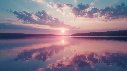 Soft clouds in shades of pink and lavender are mirrored in the still waters of the lake creating a picturesque sunset scene. - obrazy, fototapety, plakaty