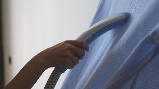 A woman steams a shirt with a hand iron and smooths out the creases on it. Housewife chores, tidying up, cleanliness, domestic lifestyle