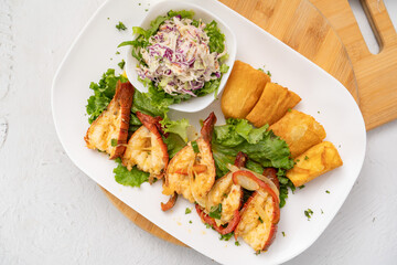 Colitas de langosta rellenas sobre una cama de lechuga acompañadas de yuca frita y ensalada sobre un plato blanco vista cenital desde arriba