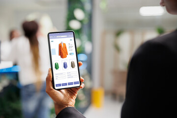 Client using clothing online web store application on smartphone, reviewing fashion items and...