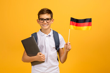 Portrait Of Happy Teen Boy With Backpack Holding German Flag And Laptop
