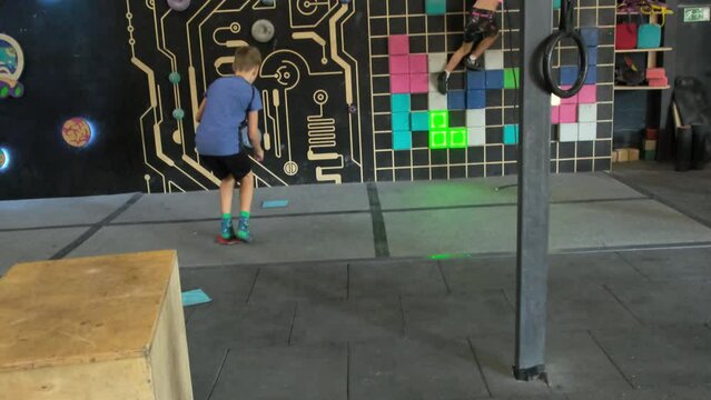 Small boy jumps off crossfit box to start climbing wall. Resilient child conqueres climbing wall with blend of strength and agility