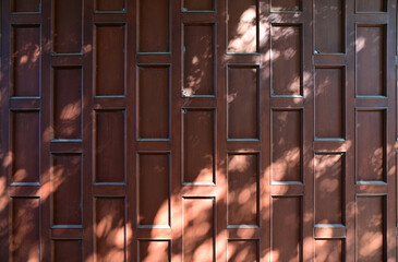 The red wooden door is closed and locked with stainless steel door knobs with the shadow of the sun...