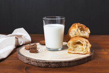 A glass of milk on a wooden table with croissants next to it.