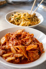 Noodles with mushrooms and vegetables and kimchi in white bowl close-up on gray background
