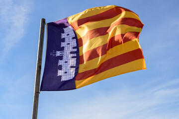 A vibrant flag with red and yellow stripes along a blue background with an emblem, against a blue...