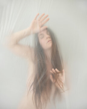 blurred, fuzzy image of sensual dreamy romantic young naked sexy woman portrait behind plastic film, playing with her hair, moves in ecstasy