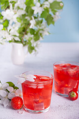 Strawberry cold refreshment lemonade with ice cube. White apple blossoms on the background. Spring concept.