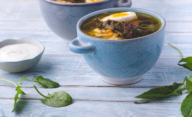 Sorrel soup or Green  spring borscht:  light soup with sorrel and egg, forest greens in spring recipes, rustic blue background. Light, dietary springtime soups