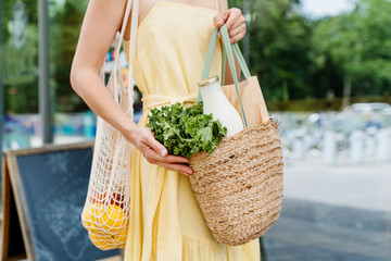 Woman holding bags with fresh organic food on storefront background of zero waste shop.