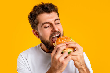 Closeup of hungry man savoring a tasty hamburger, yellow background