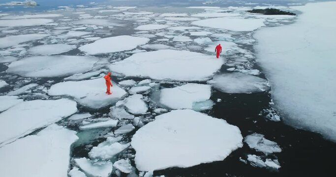 People in immersion suits on melted arctic ice. Two man in orange wetsuits stuck in polar trap try to run melting winter ocean cold water. Explore global climate warming melt glaciers. Aerial panorama
