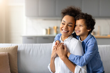 Smiling black mother and son enjoying happy embrace at home, looking at free space