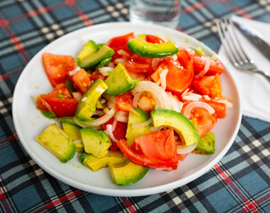Traditional vegetarian salad from fresh ripe avocado with tomatoes and sliced onions dressed with oil.