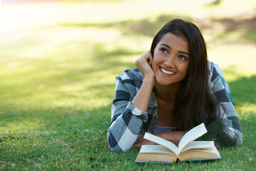Woman, thinking and reading book on grass, literature and smiling for fiction or fantasy story....