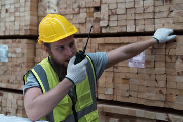Male warehouse worker using radio communication checks stock inventory in lumber storage warehouse....