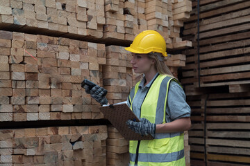 Woman warehouse worker scanning barcodes on pile of plank wooden in lumber storage warehouse. Woman...