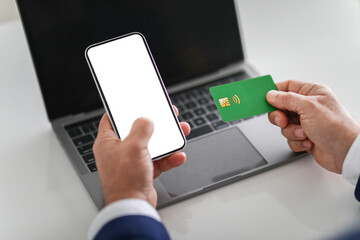 Businessperson holding a smartphone with a blank screen in one hand and a green credit card